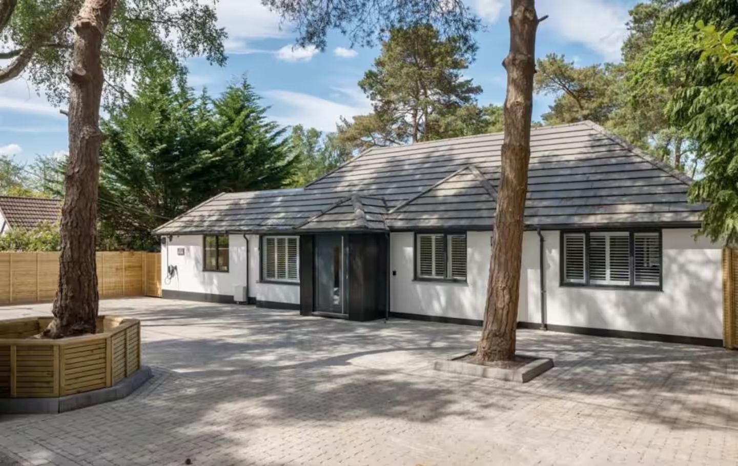 The front of Kiwi Pines, with a wide block-paved drive and parking for several cars